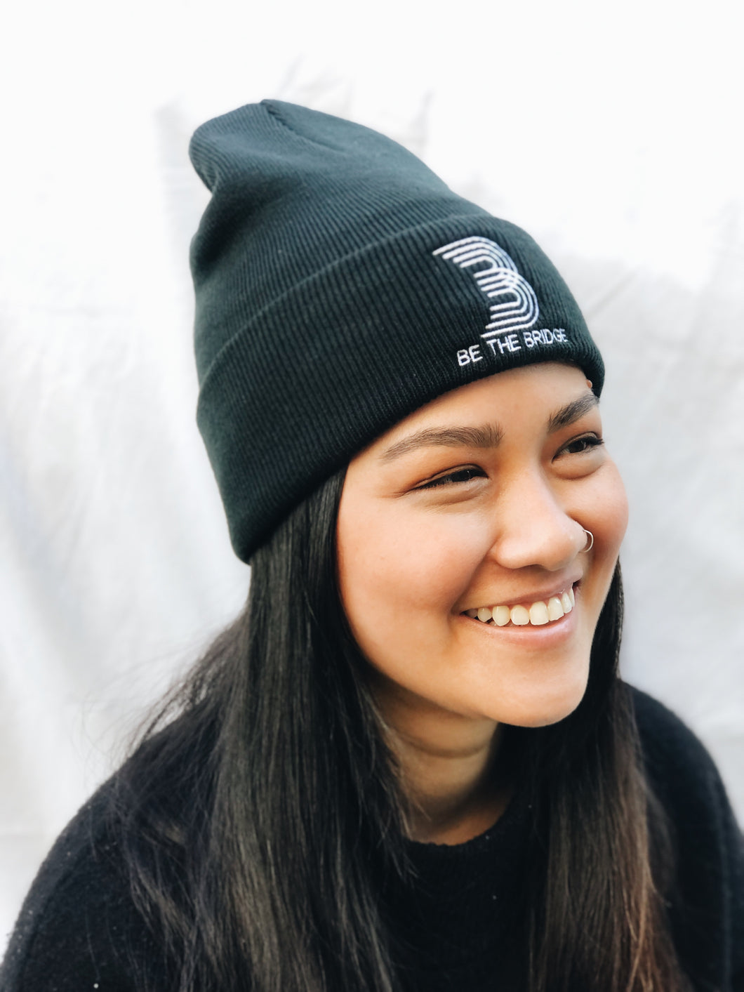 Woman wearing black beanie with 'B' and 'Be the Bridge' in white lettering.