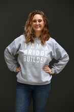 Woman wearing gray sweatshirt with 'I Am A Bridge Builder' in white lettering.