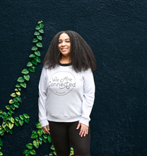 Woman wearing a gray sweatshirt with 'We Are Connected' 'Be the Bridge' written in black lettering inside of a black circle outline.